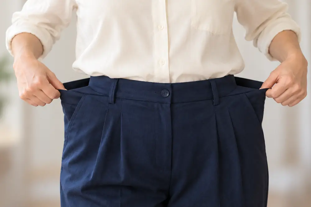 Woman holding out loose-fitting trousers after medically supervised weight loss